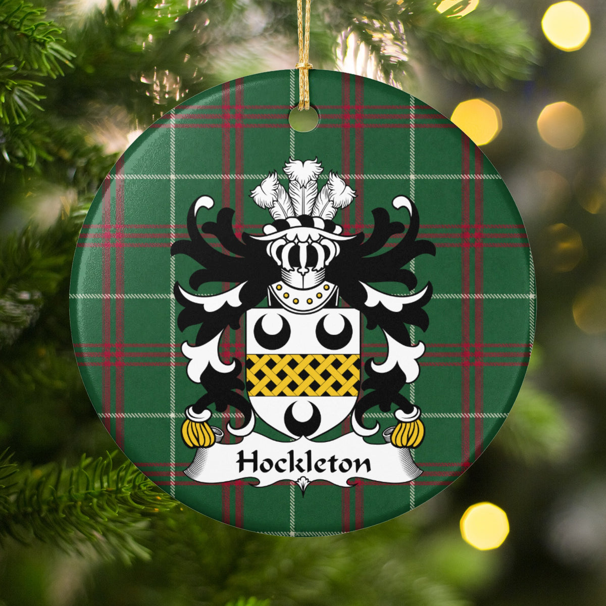 Hockleton ornament hanging in a Christmas tree with warm lights; a white shield with three black crescents and a gold lattice band on Welsh national tartan.