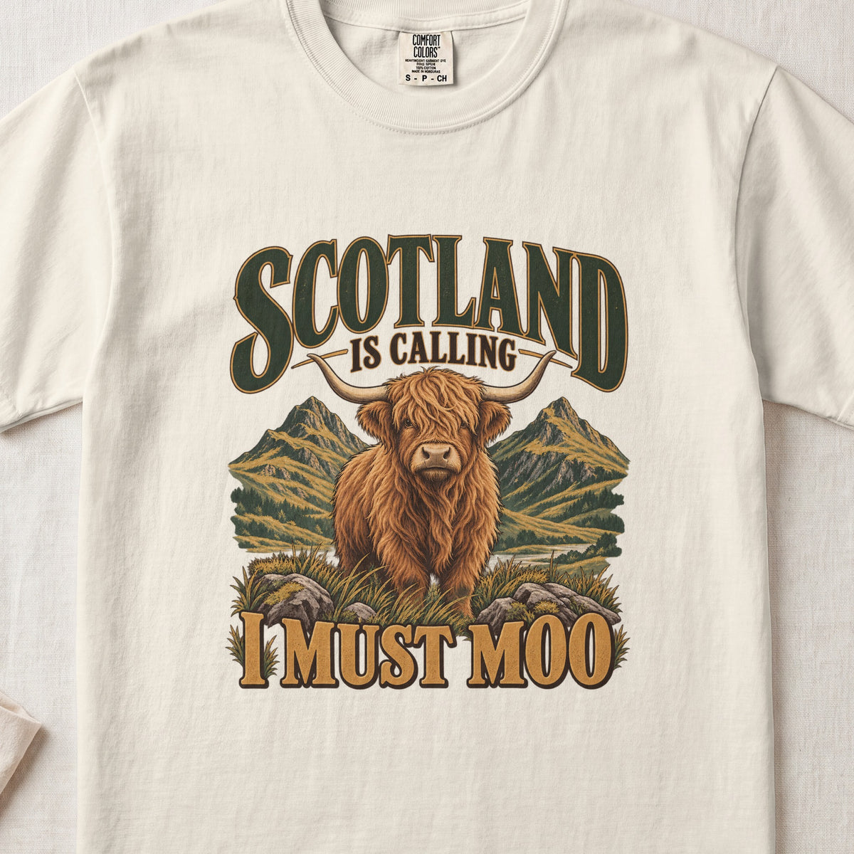 Scotland Is Calling, I Must Moo Highland cow design on an Ivory Comfort Colors 1717 T-shirt, flat lay