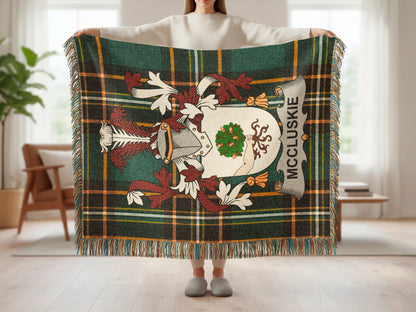 Tartan blanket with McCluskie clan crest and decorative border held by a person.