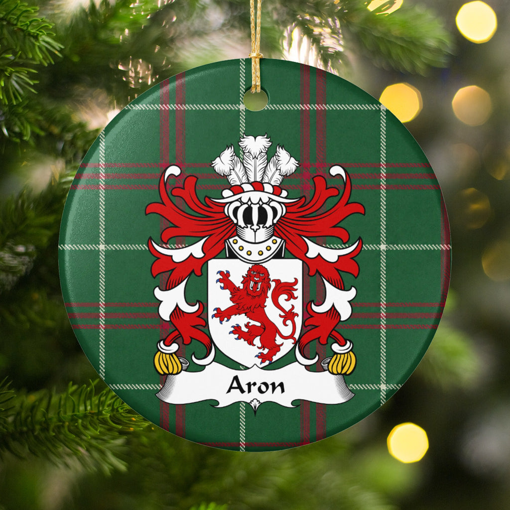 Aron family crest and surname on a round Welsh national tartan ornament, hanging by a gold cord among Christmas tree branches and warm golden lights.