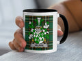 White mug with black handle featuring a green and white plaid background and a coat of arms.