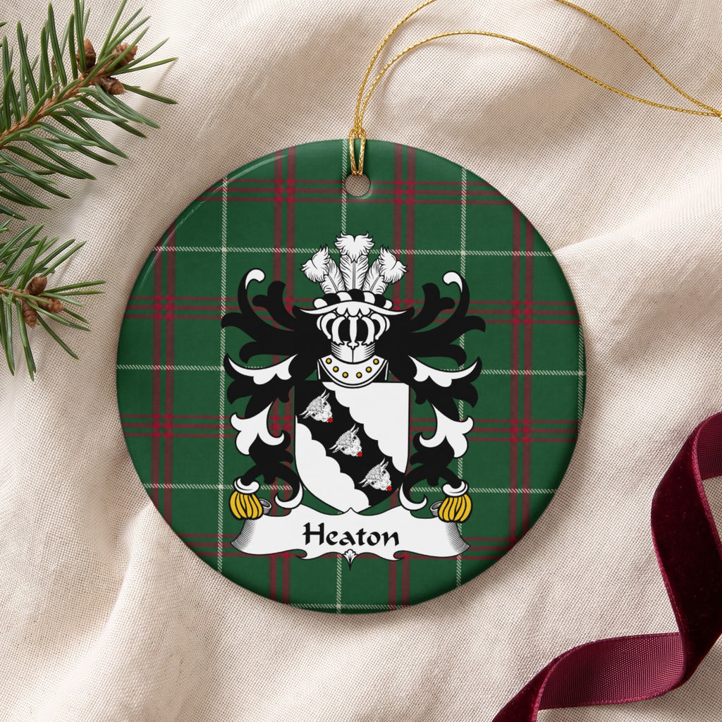 Heaton ornament on cream fabric beside evergreen and burgundy ribbon, with gold string; three white bull heads on a scalloped black diagonal band across a white shield.