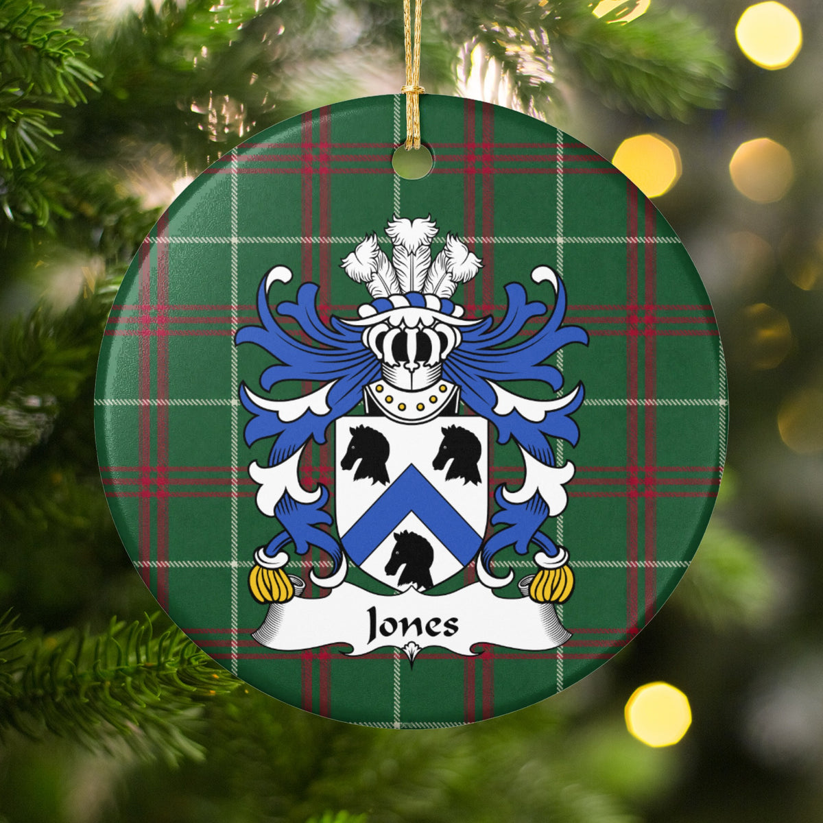 Jones Style 3 ornament hanging on a Christmas tree among green branches and warm lights, with a white shield with a blue chevron and three black animal heads on Welsh national tartan.