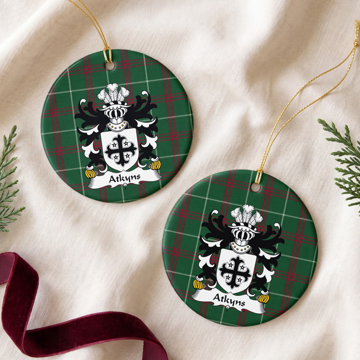 Two Atkyns ornaments on cream fabric with evergreen and burgundy ribbon; a black decorative cross surrounded by four small black stars on white on Welsh national tartan.
