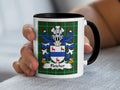 Mug with Fletcher coat of arms on green tartan background held by hand.