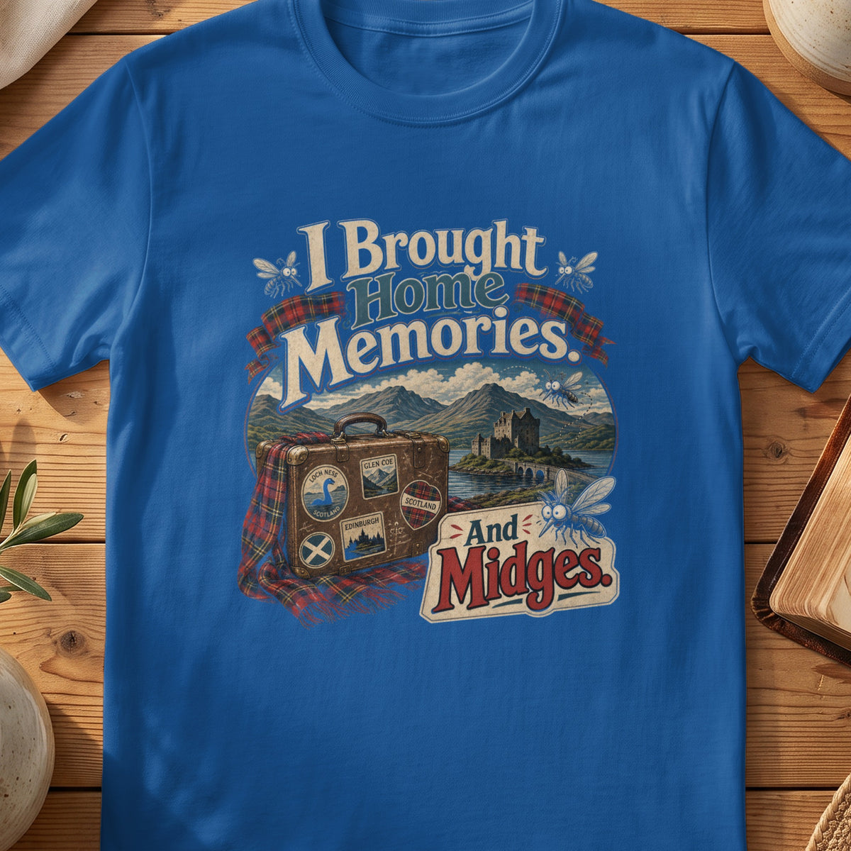 Blue t-shirt with graphic "I Brought Home Memories. And Midges." and suitcase.