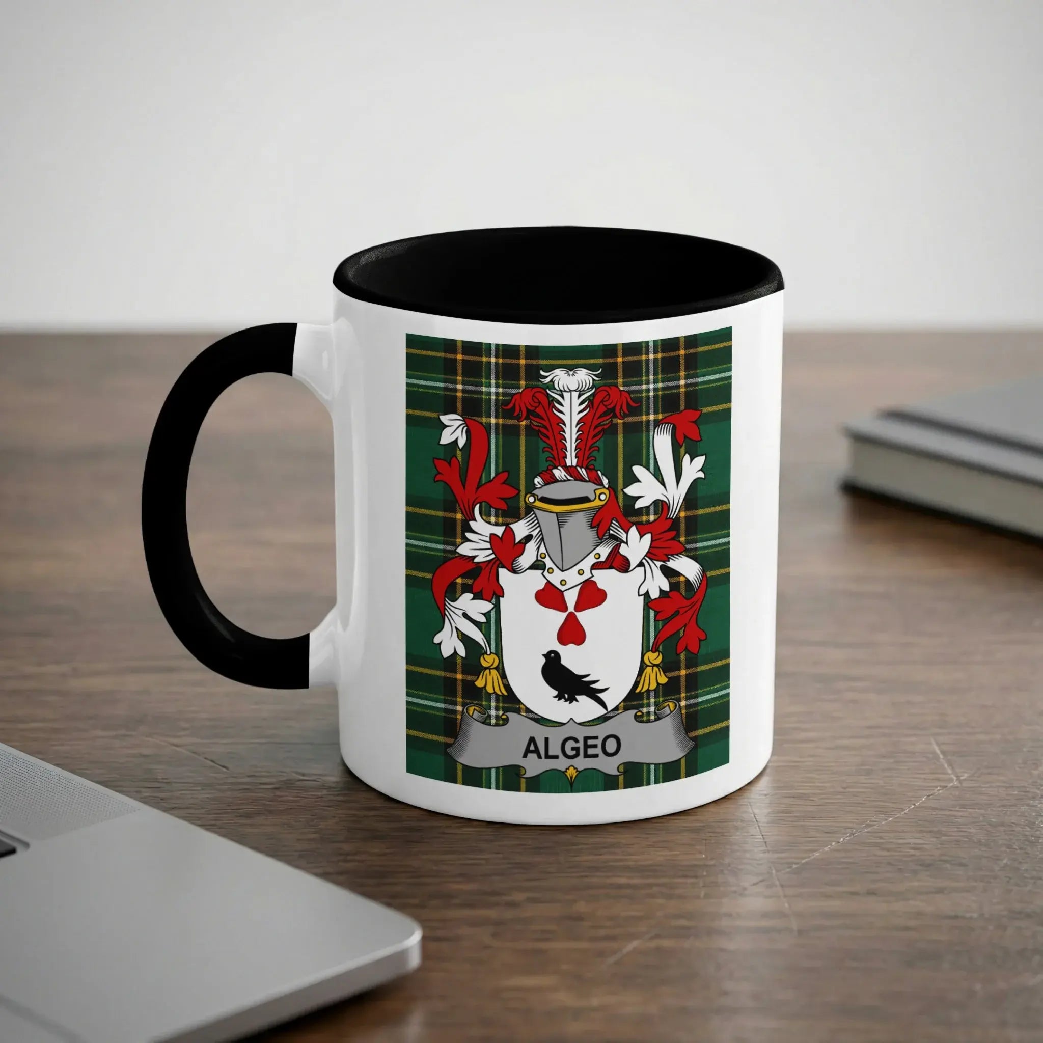 White mug with black rim featuring the Algeo coat of arms on a wooden desk.