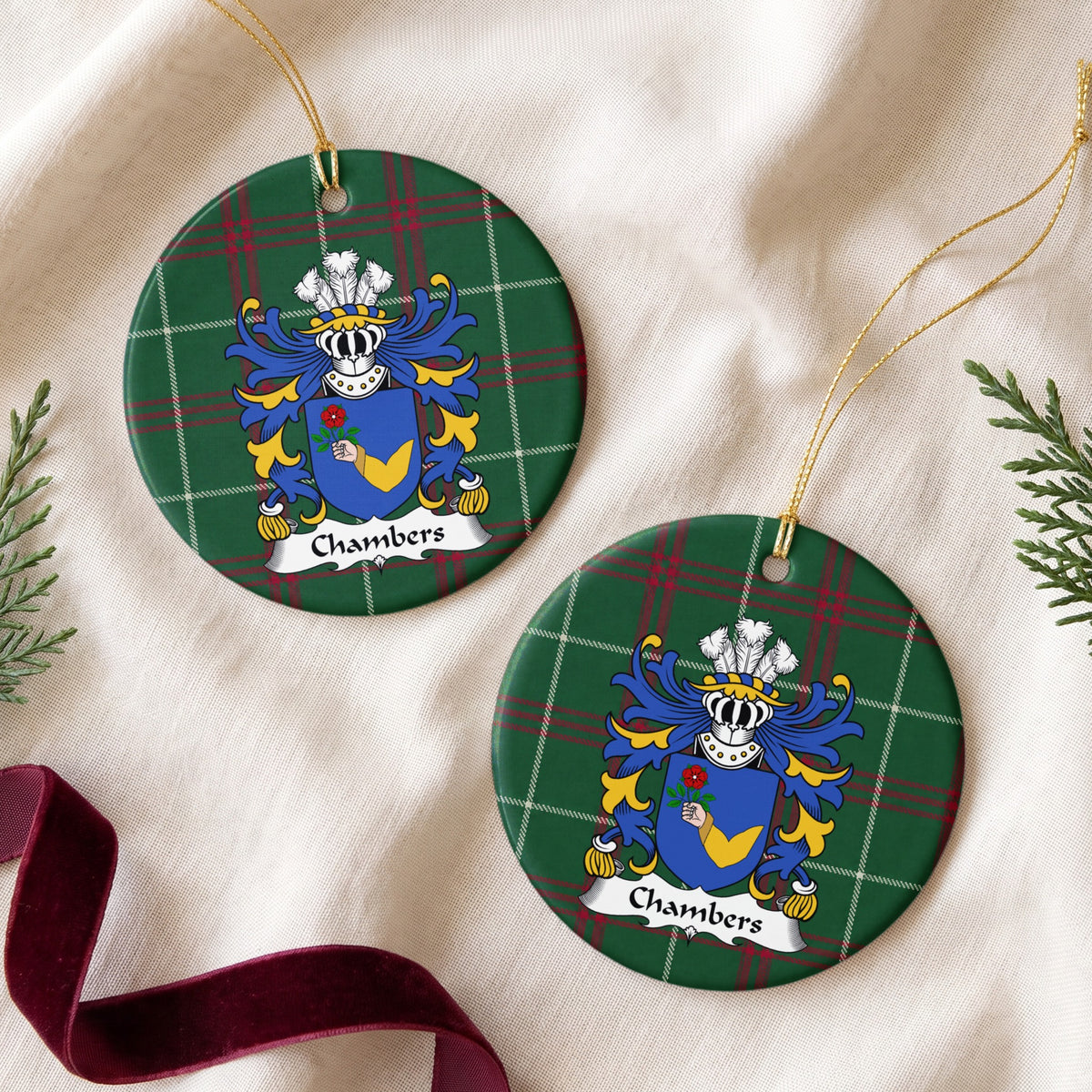 Two Chambers ornaments on cream fabric beside evergreen sprigs and burgundy ribbon; a hand in a gold sleeve holding a red rose on a blue shield on Welsh national tartan.