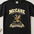 McCabe Scottish clan T-shirt in Black, front view with a brown and gold winged griffin with green claws and motto banner.