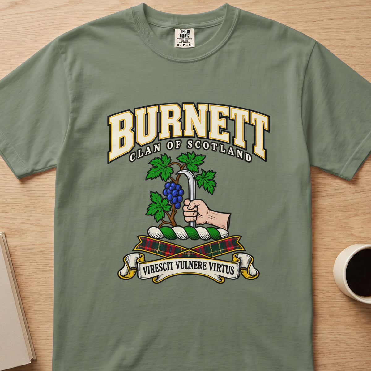 Burnett clan crest with grapevine and pruning hook on a sage green Comfort Colors T-shirt, front view