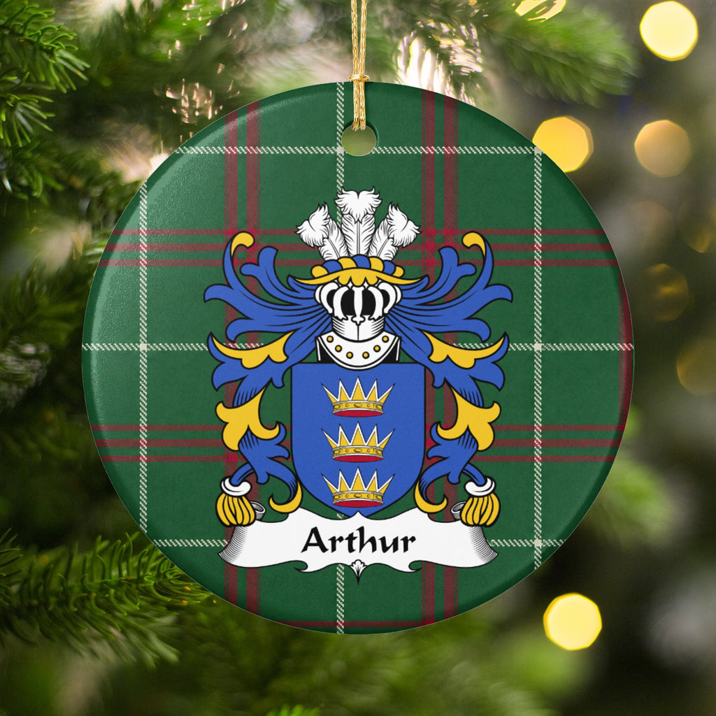 Arthur family crest and surname on a round Welsh national tartan ornament, hanging by a gold cord among Christmas tree branches and warm golden lights.