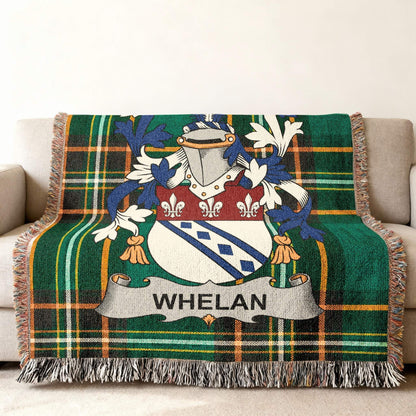 Green plaid woven throw blanket with Whelan family crest on couch.