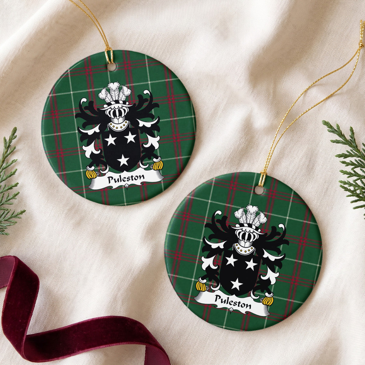 Puleston round Welsh National Tartan ornament shown as a pair on cream fabric with evergreen sprigs and burgundy ribbon, featuring three white stars on a black shield.