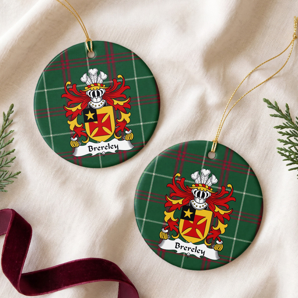 Two Brereley ornaments on cream fabric beside evergreen and burgundy ribbon; a red flared cross on gold with a gold star in a black corner panel on Welsh national tartan.