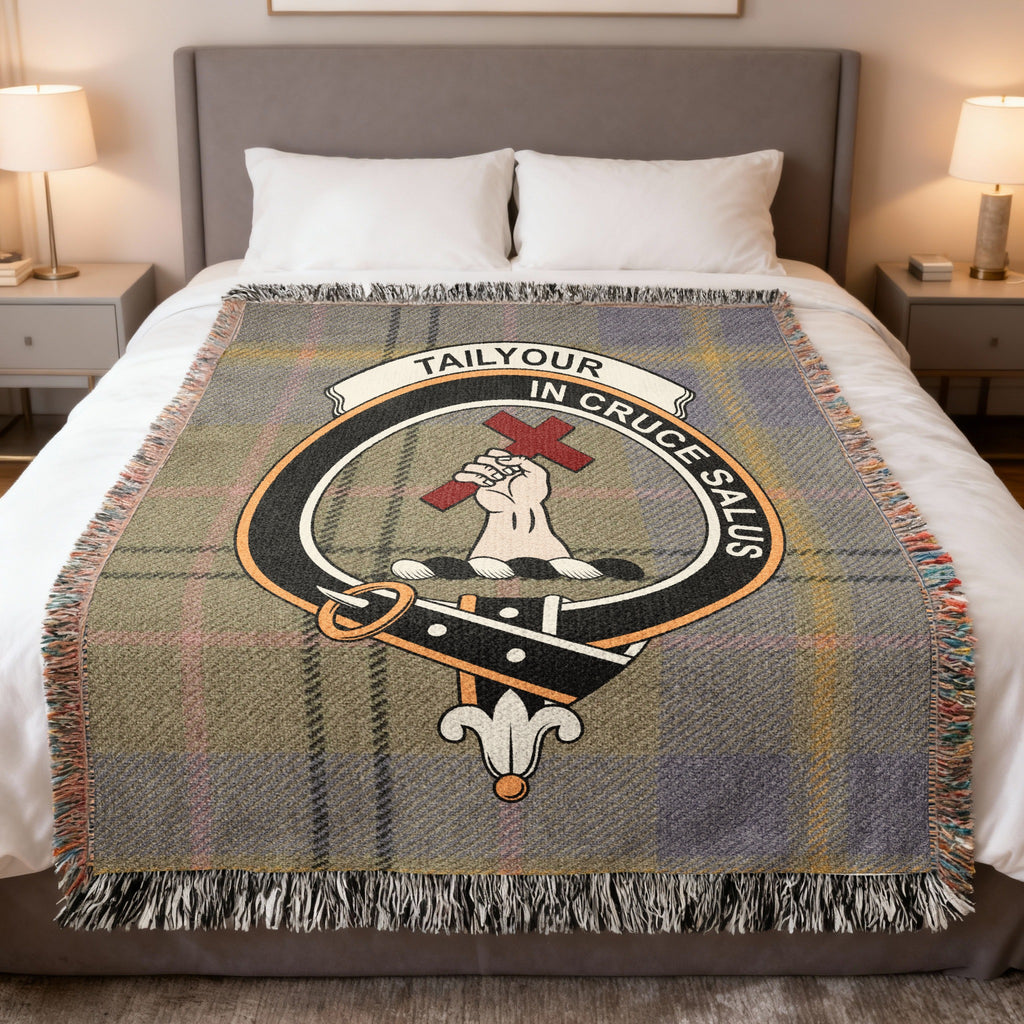 Tailyour woven blanket displayed on a bed, with a hand holding a red cross on a muted grey, green and blue tartan background