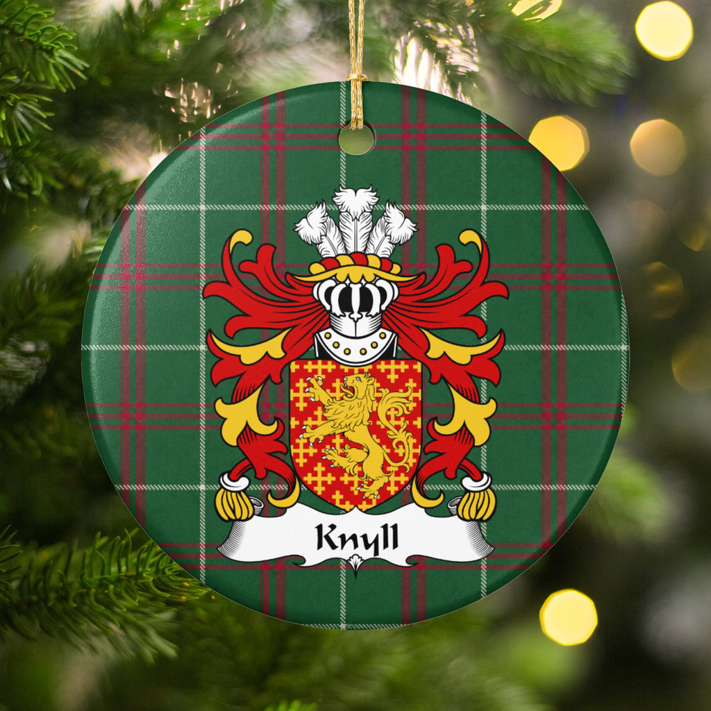Knyll ornament hanging on a Christmas tree among green branches and warm lights, with a red shield with a gold lion surrounded by small gold crosses on Welsh national tartan.