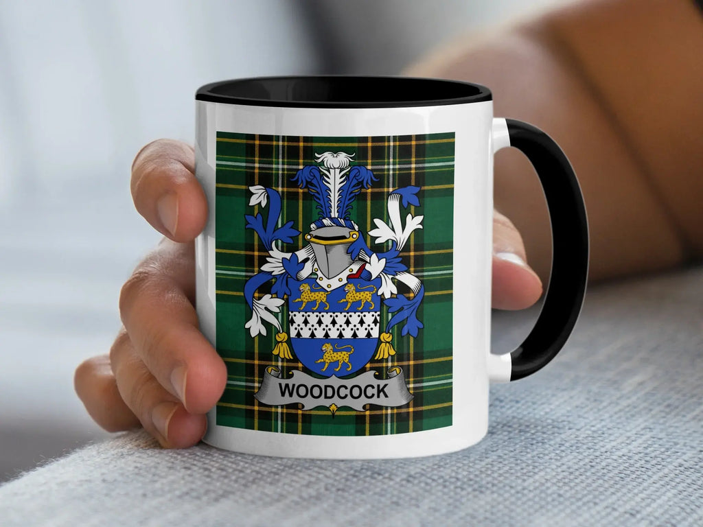 White mug with black rim featuring a blue and gold Woodcock family crest on plaid background.