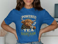 Blue t-shirt with highland cow graphic, "Powered by Tea and Sarcasm" text.