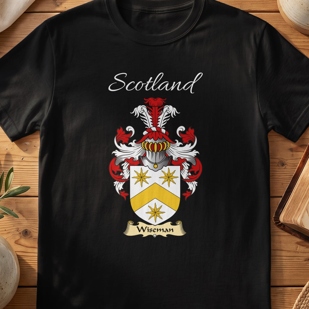 Black Wiseman Scottish family crest T-shirt laid flat, showing “Scotland” above a gold-and-silver shield with a radiant star and angular divisions.