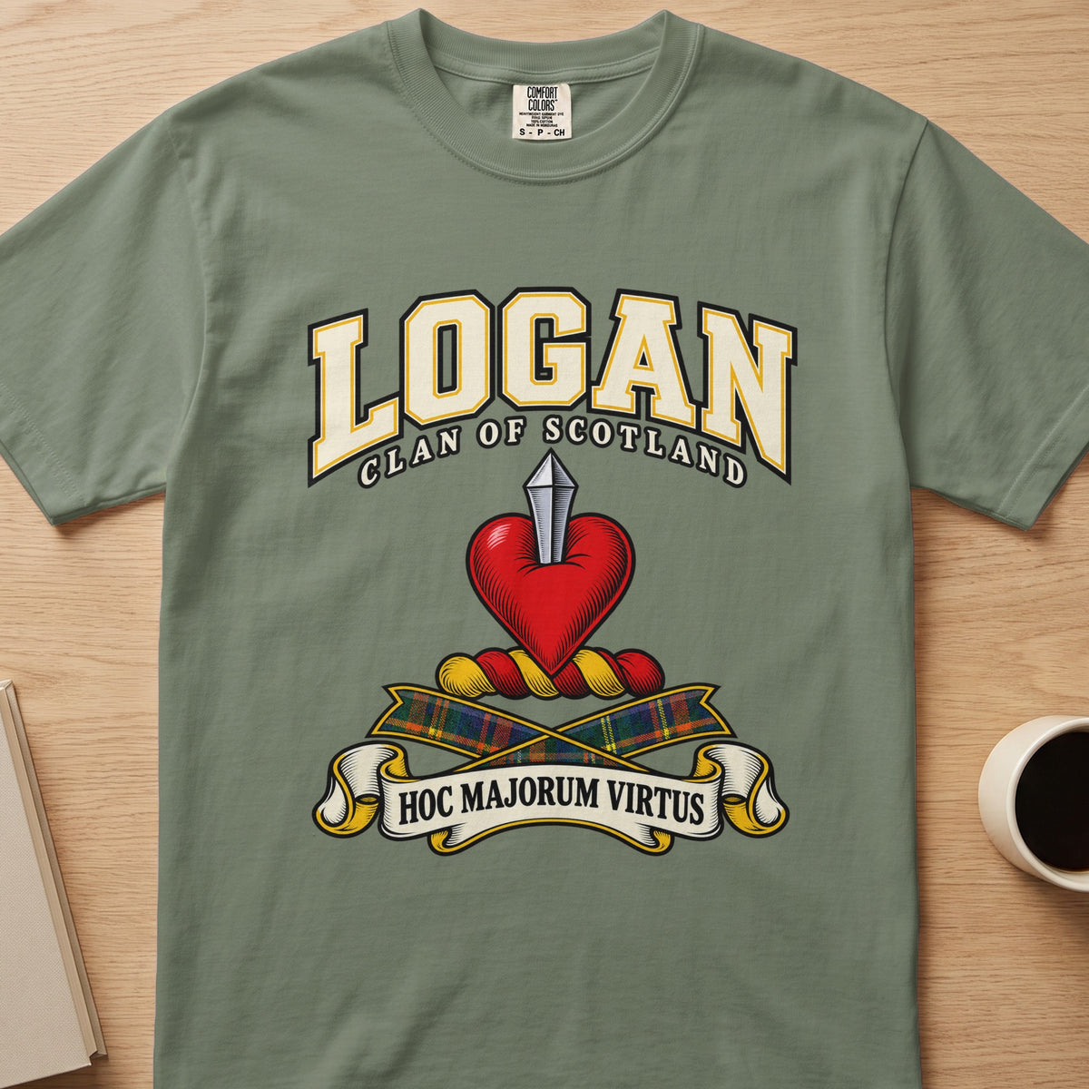 Logan clan crest with red heart and silver blade on a sage green Comfort Colors T-shirt, front view