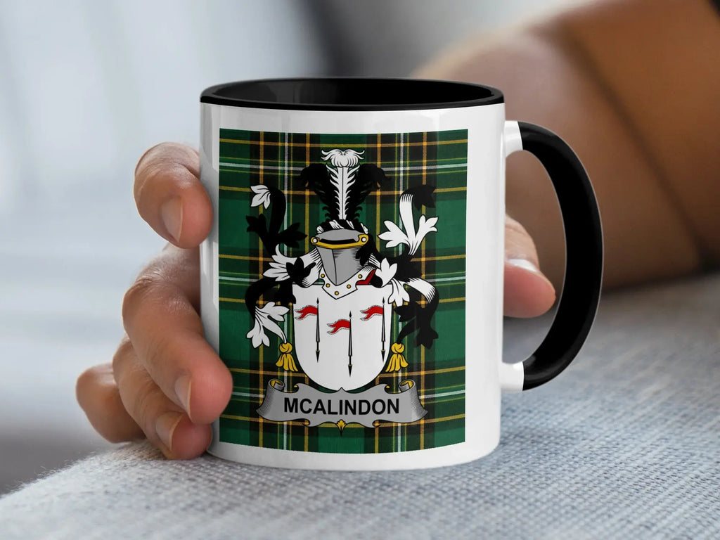 Mug with black handle and rim displaying the McAlindon family crest on a tartan background.