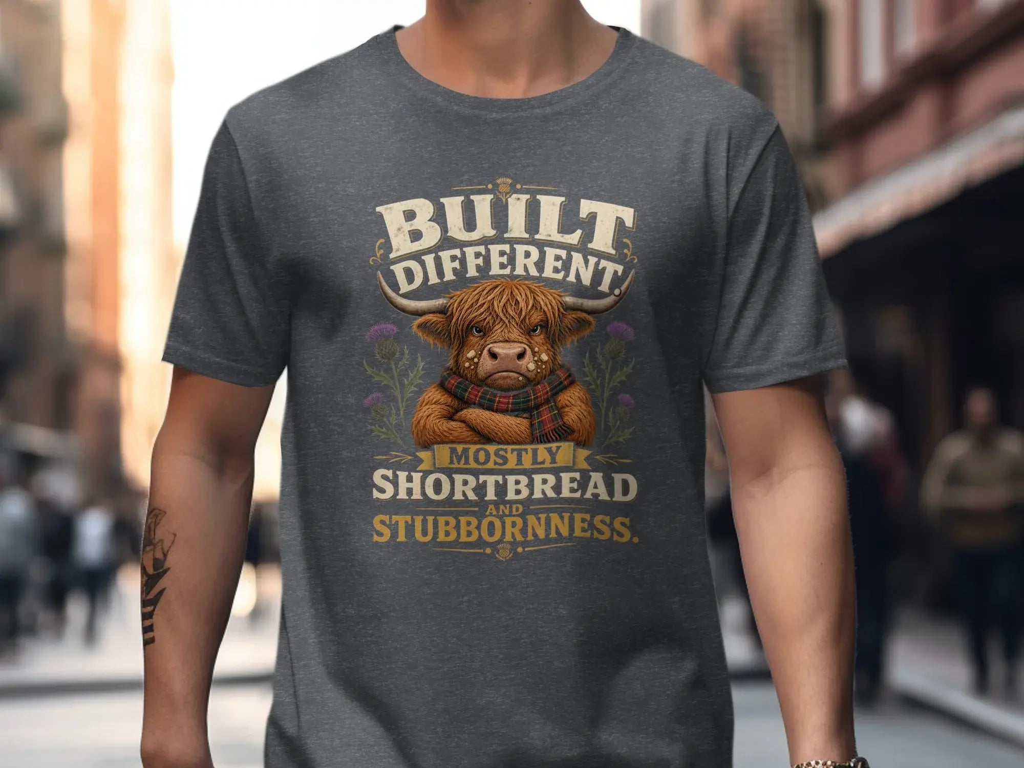 T-shirt with a Highland cow graphic and text "BUILT DIFFERENTLY MOSTLY SHORTBREAD AND STUBBORNNESS".