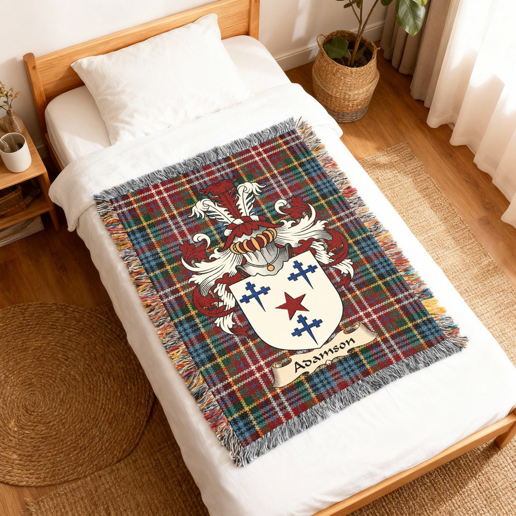 Adamson Scottish family shield woven blanket with Caledonia tartan background, displayed on a bed