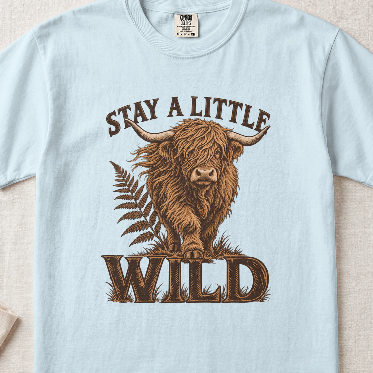 Stay a Little Wild Highland cow design on a Chambray Comfort Colors 1717 T-shirt, flat lay