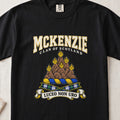 McKenzie graphic T-shirt in Black, front flat lay showing varsity lettering and brown rocky mountain-like mound with yellow flames.