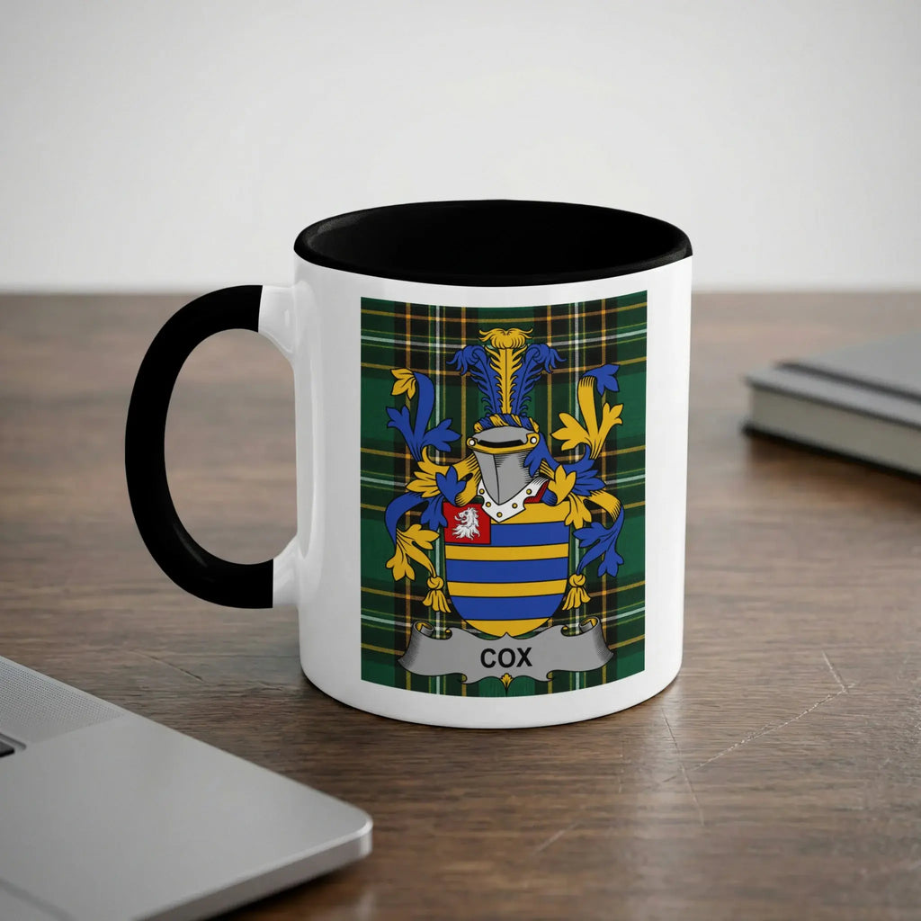White mug with black handle displaying the COX family crest on a tartan background.