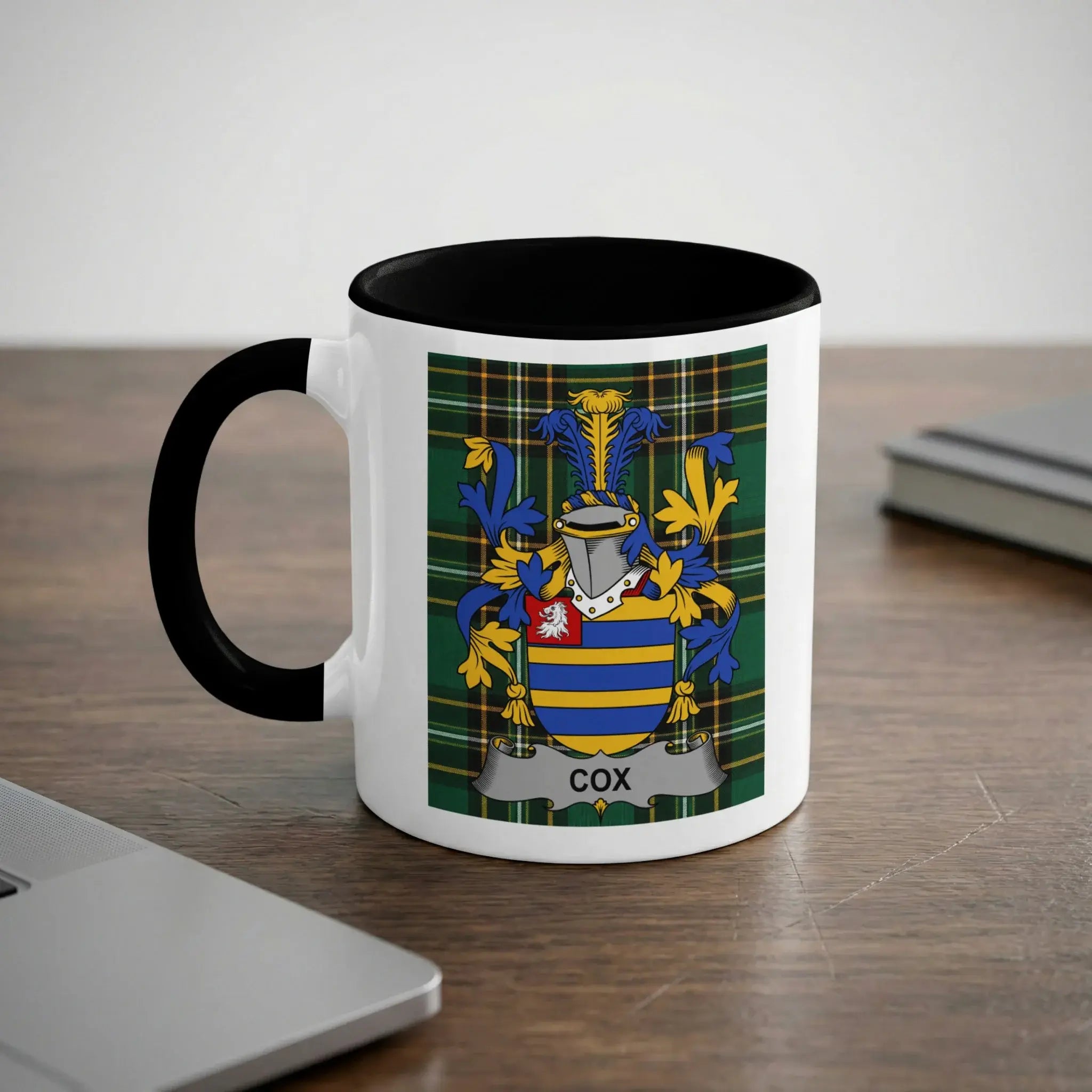 White mug with black handle displaying the COX family crest on a tartan background.