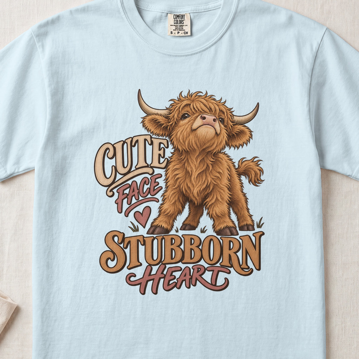 Cute Face, Stubborn Heart Highland cow design on a Chambray Comfort Colors 1717 T-shirt, flat lay