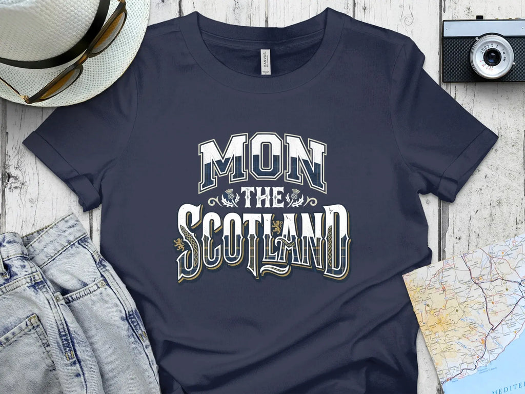 Dark blue t-shirt with "MON THE SCOTLAND" text, flat lay with jeans and camera.