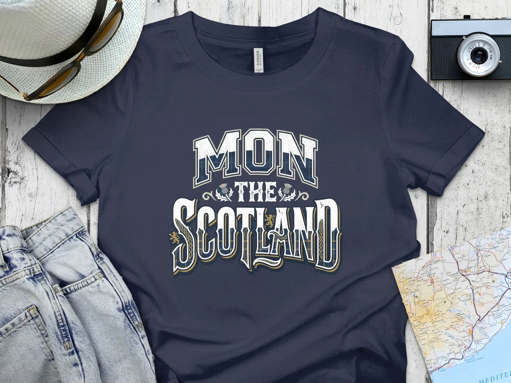 Dark blue t-shirt with "MON THE SCOTLAND" text, flat lay with jeans and camera.