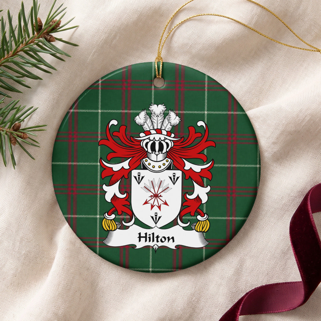 Hilton ornament on cream fabric beside evergreen and burgundy ribbon, with gold string; a tied bundle of arrows and three black arrowheads on a white shield.