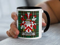 White mug with Maynard family crest on plaid background.