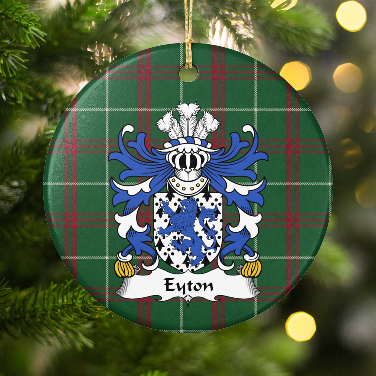 Eyton ornament hanging among Christmas tree branches and warm lights; a blue lion on a white shield patterned with black ermine marks on Welsh national tartan.