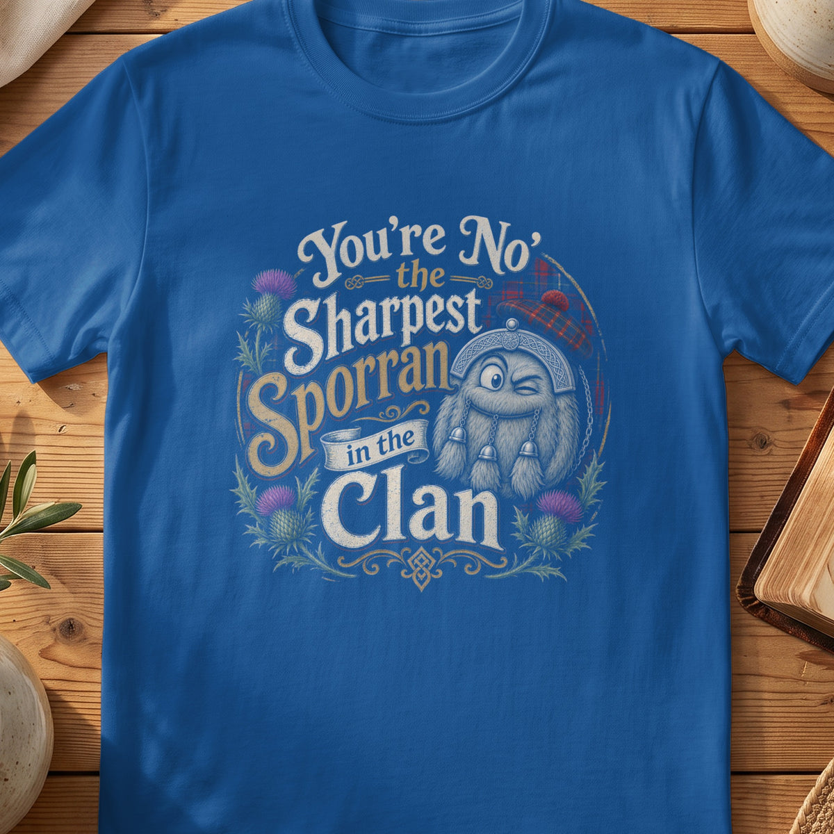 Blue t-shirt with a graphic of a cartoon sporran saying "You're No' the Sharpest Sporran in the Clan".
