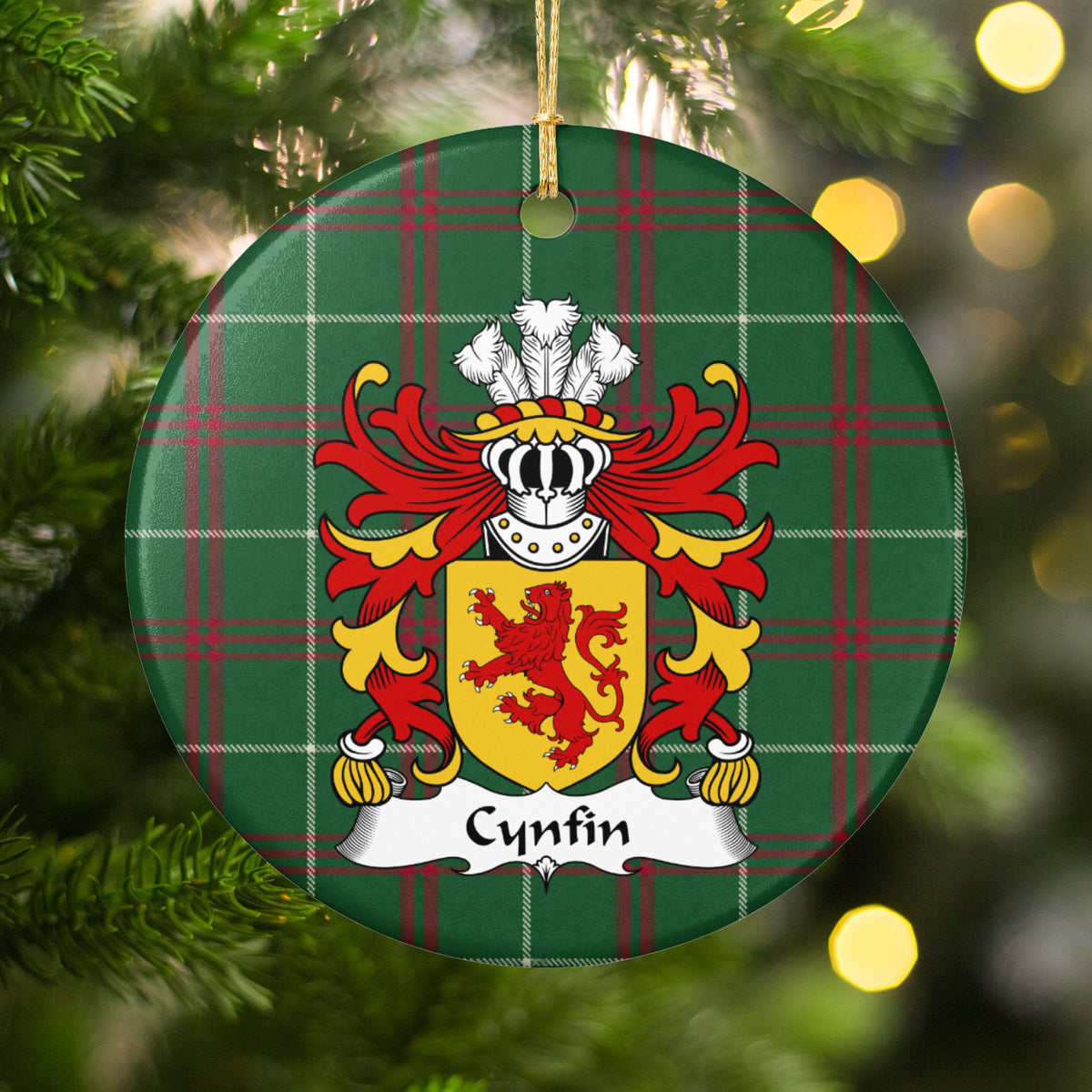 Cynfin ornament hanging among Christmas tree branches and warm lights; a red upright lion on a gold shield on Welsh national tartan.