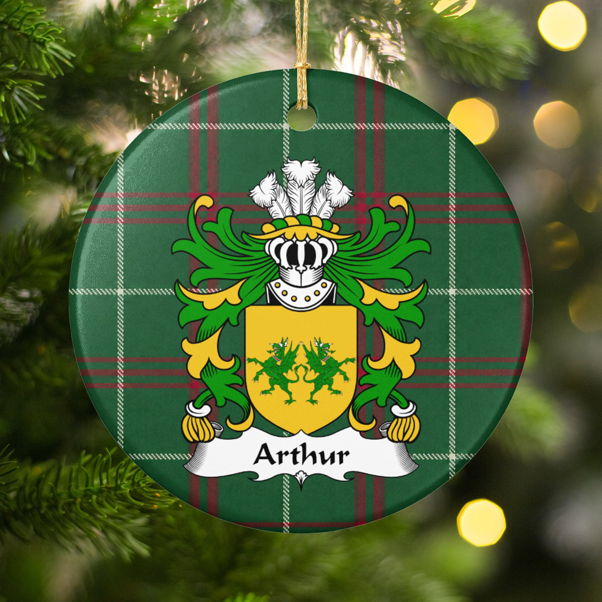 Arthur family crest and surname on a round Welsh national tartan ornament, hanging by a gold cord among Christmas tree branches and warm golden lights.