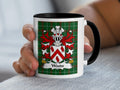 Mug with Woods family crest on green plaid background, held by a hand.