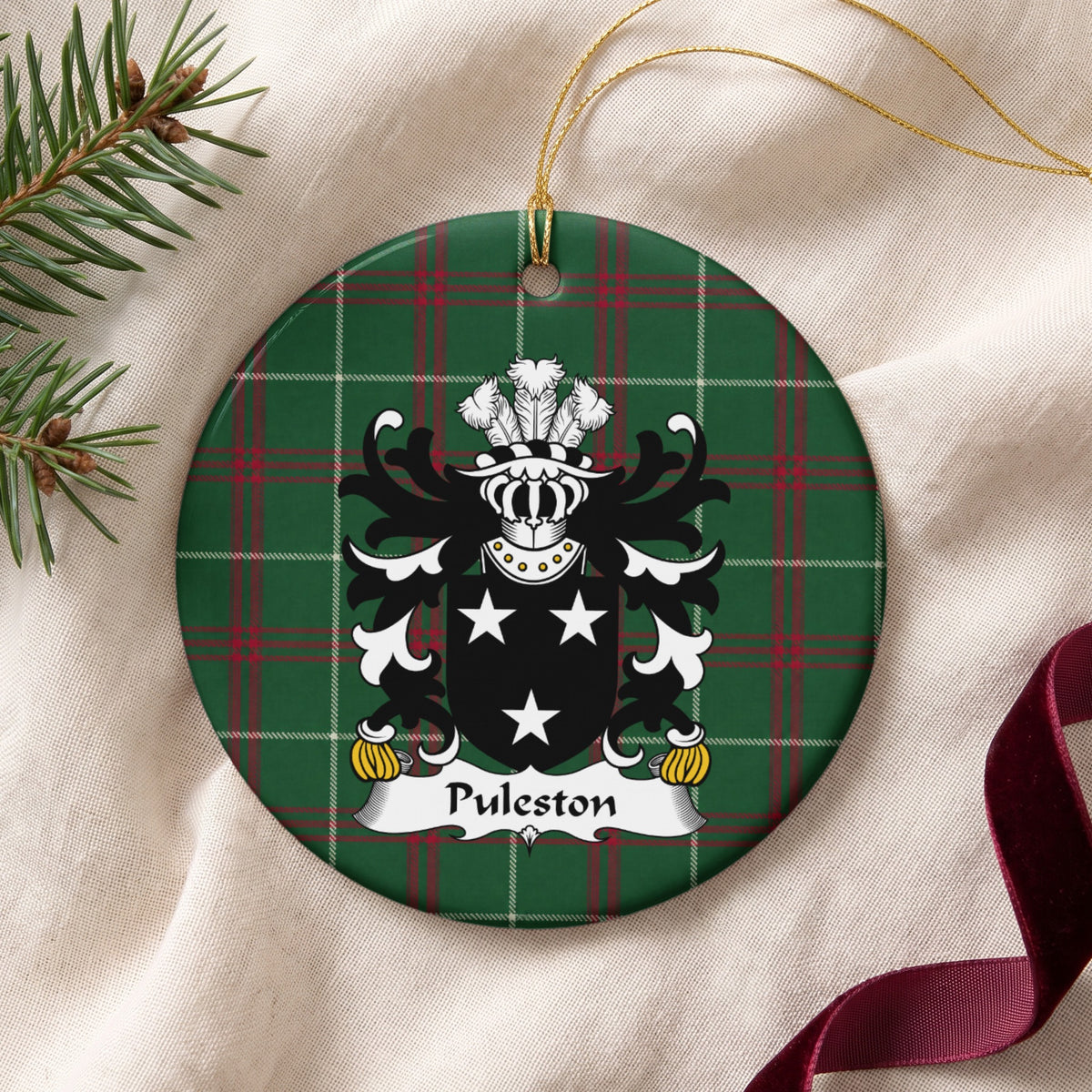 Puleston round Welsh National Tartan ornament lying on cream fabric beside evergreen and burgundy ribbon, featuring three white stars on a black shield.