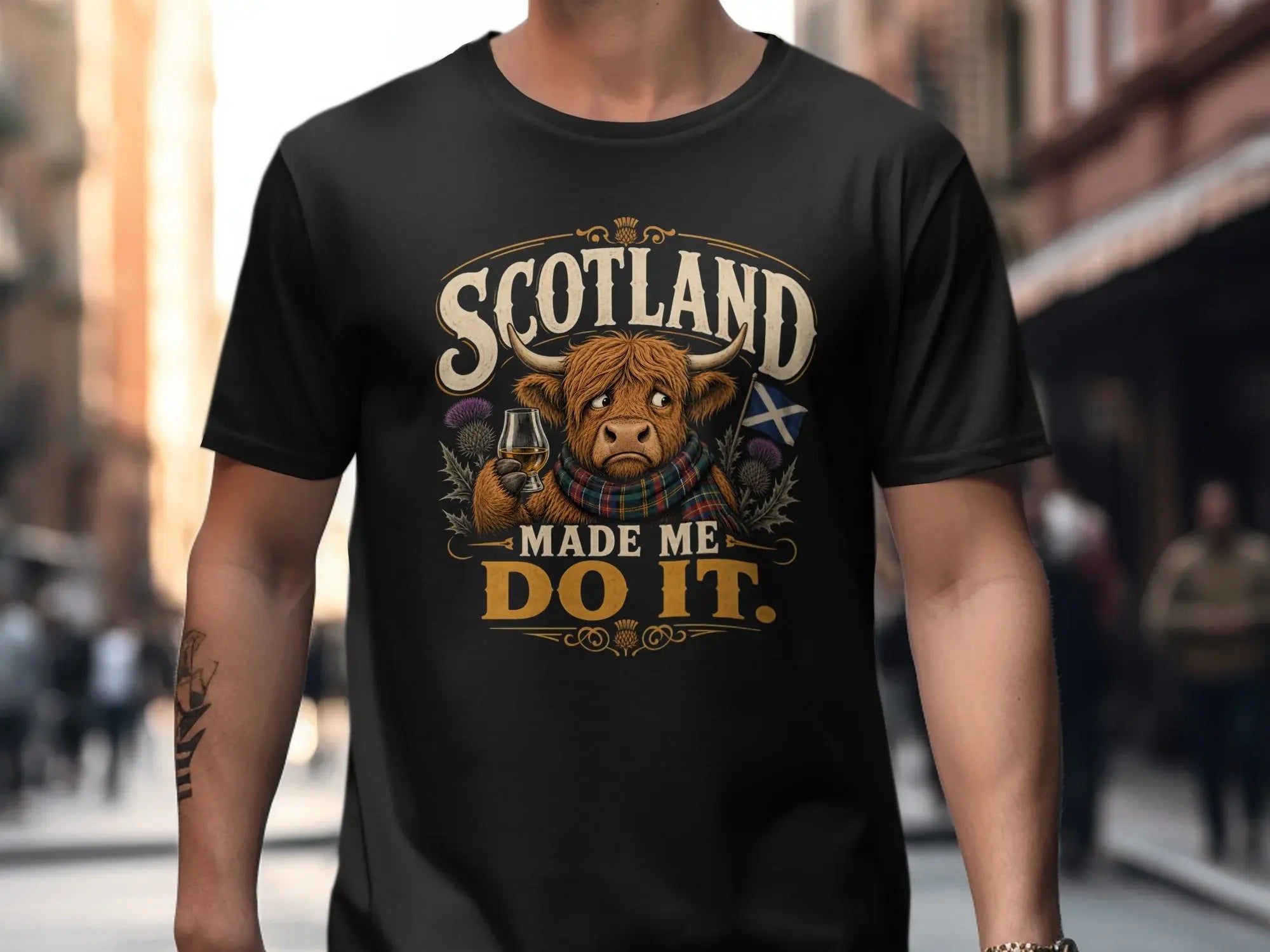 Black t-shirt with "Scotland Made Me Do It" text, a Highland cow, and Scottish flag.