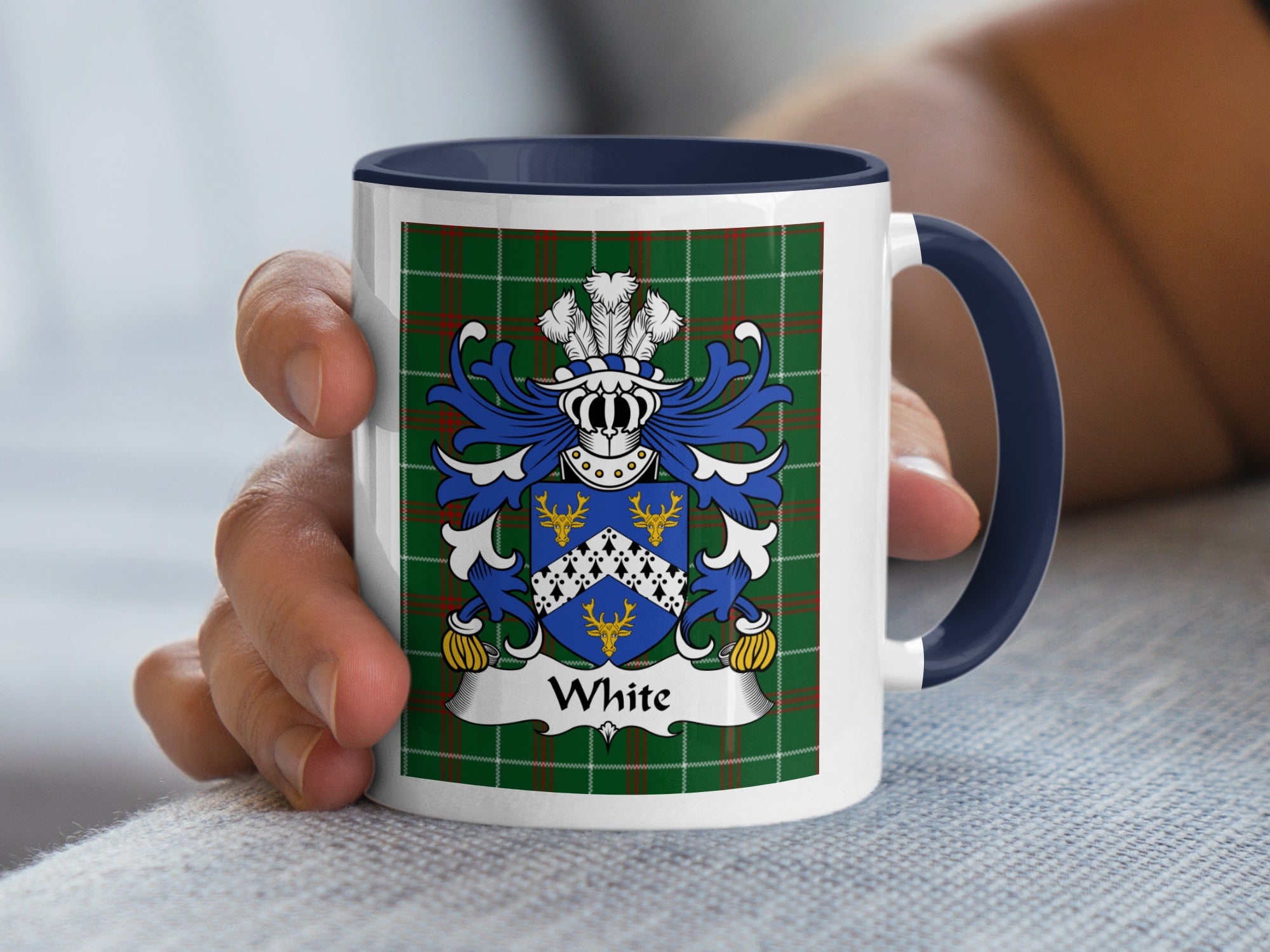Mug with White family crest on green tartan background held by hand.