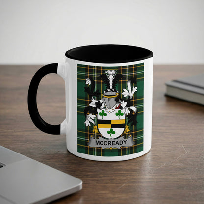 White mug with black handle featuring McCready family crest on tartan background.