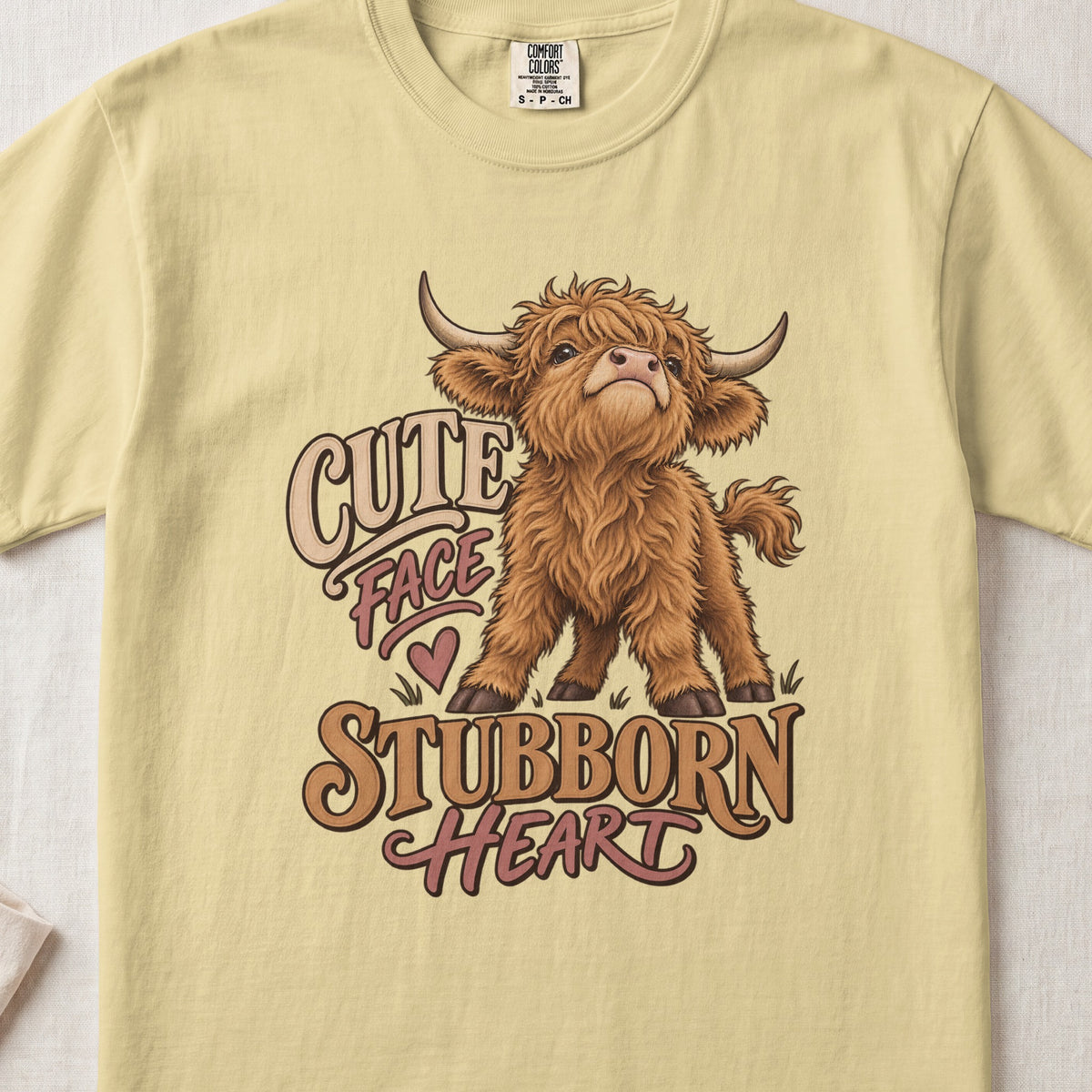 Cute Face, Stubborn Heart Highland cow design on a Butter Comfort Colors 1717 T-shirt, flat lay