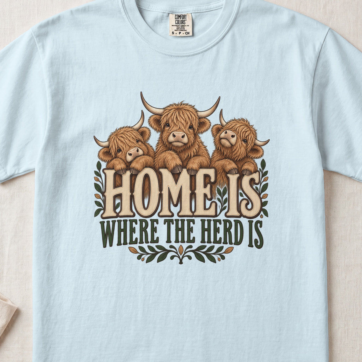 Home Is Where the Herd Is Highland cow design on a Chambray Comfort Colors 1717 T-shirt, flat lay