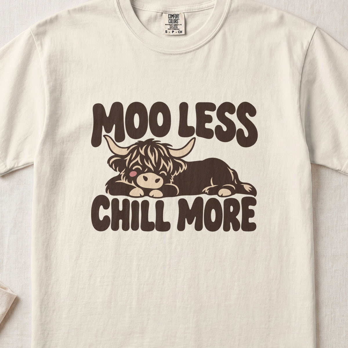 Moo Less, Chill More Highland cow design on an Ivory Comfort Colors 1717 T-shirt, flat lay
