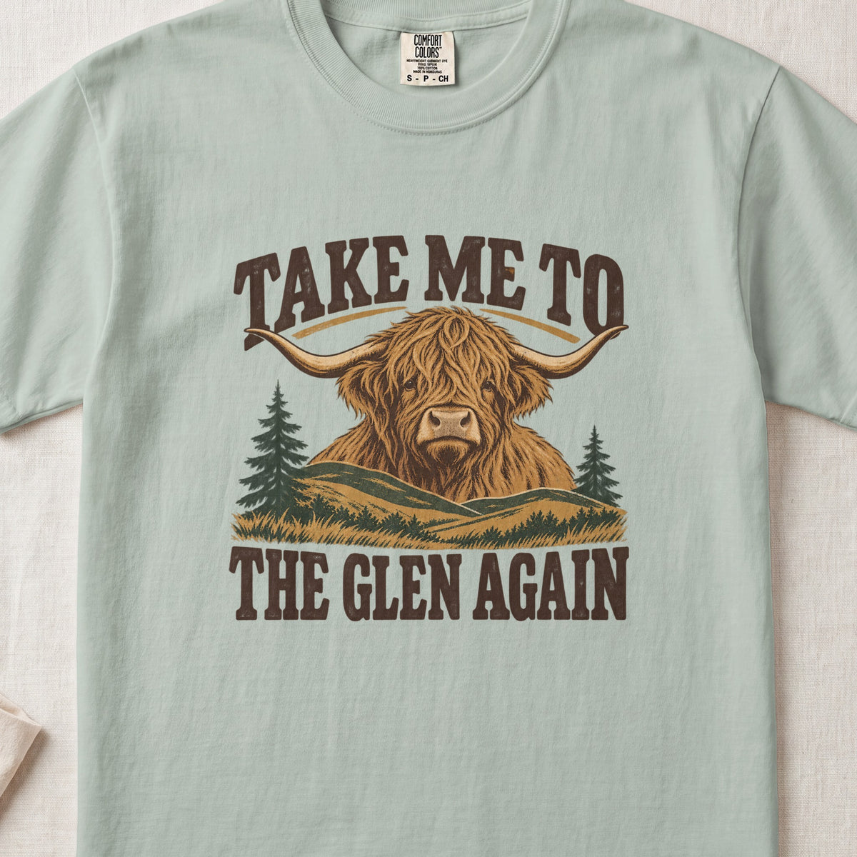 Take Me to the Glen Again Highland cow design on a Bay Comfort Colors 1717 T-shirt, flat lay