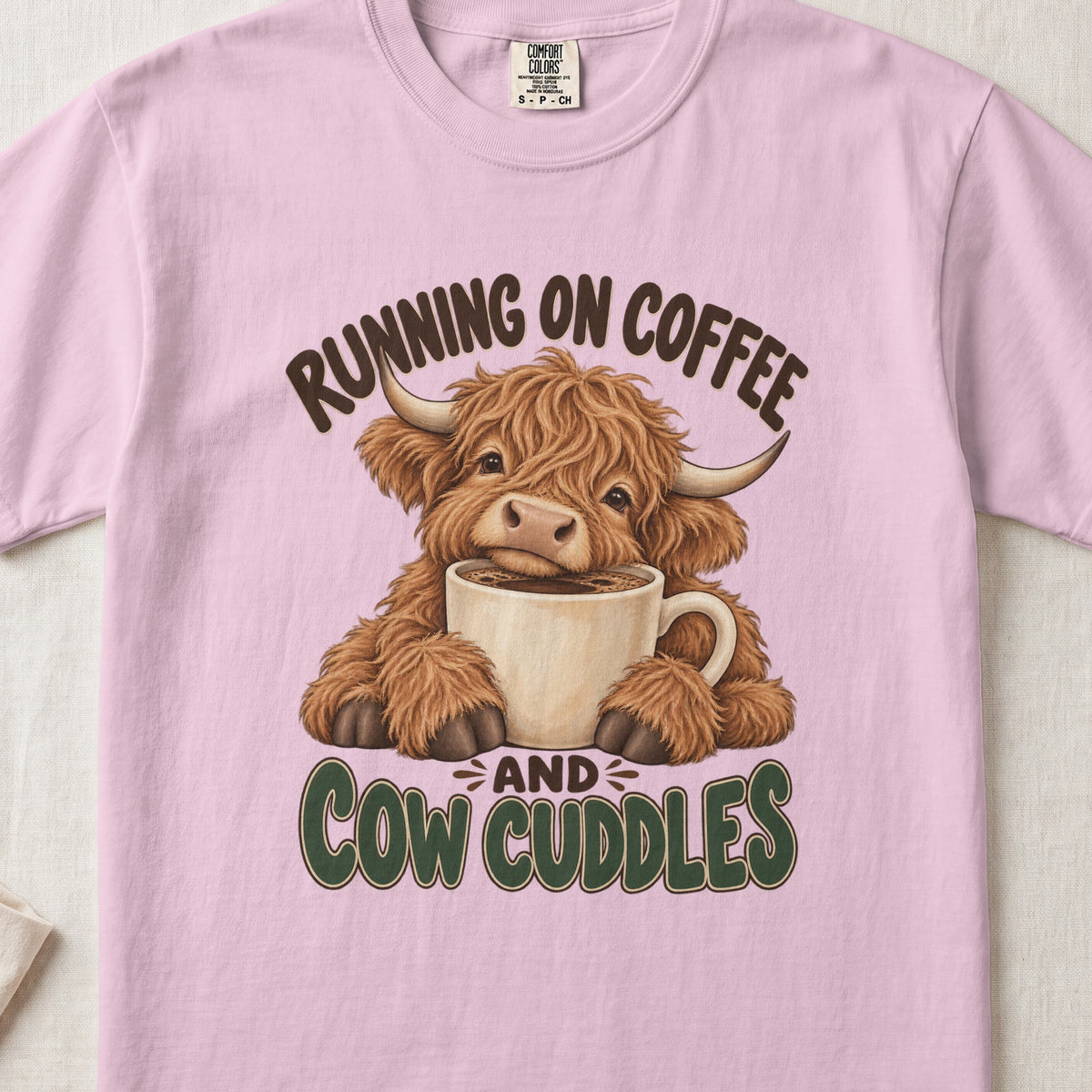 Running on Coffee & Cow Cuddles Highland cow design on a Blossom Comfort Colors 1717 T-shirt, flat lay
